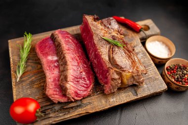 Siyah taş arka plan üzerinde ahşap doğrama tahtası üzerinde baharat ile Taze nadir ızgara beefsteak