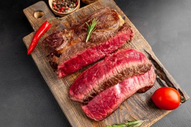 Siyah taş arka plan üzerinde ahşap doğrama tahtası üzerinde baharat ile Taze nadir ızgara beefsteak