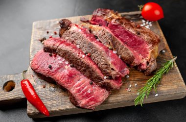 Siyah taş arka plan üzerinde ahşap doğrama tahtası üzerinde baharat ile Taze nadir ızgara beefsteak