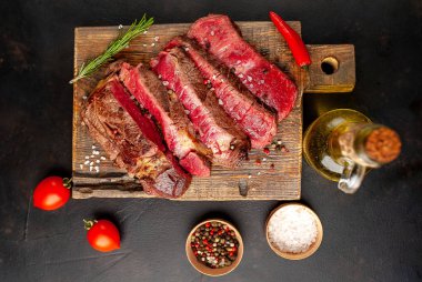 Siyah taş arka plan üzerinde ahşap doğrama tahtası üzerinde baharat ile Taze nadir ızgara beefsteak