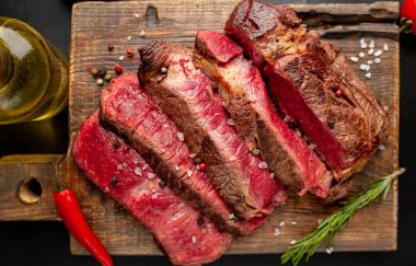 Siyah taş arka plan üzerinde ahşap doğrama tahtası üzerinde baharat ile Taze nadir ızgara beefsteak