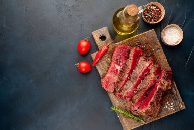 Siyah taş arka plan üzerinde ahşap doğrama tahtası üzerinde baharat ile Taze nadir ızgara beefsteak