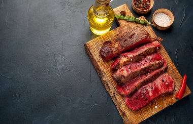 Siyah taş arka plan üzerinde ahşap doğrama tahtası üzerinde baharat ile Taze nadir ızgara beefsteak