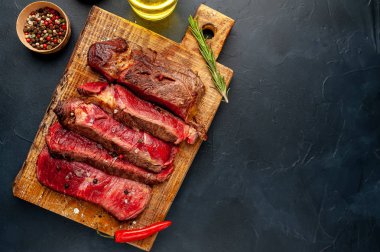 Siyah taş arka plan üzerinde ahşap doğrama tahtası üzerinde baharat ile Taze nadir ızgara beefsteak