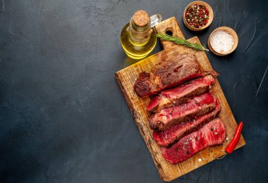 Siyah taş arka plan üzerinde ahşap doğrama tahtası üzerinde baharat ile Taze nadir ızgara beefsteak
