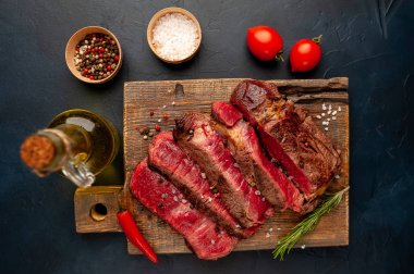 Siyah taş arka plan üzerinde ahşap doğrama tahtası üzerinde baharat ile Taze nadir ızgara beefsteak