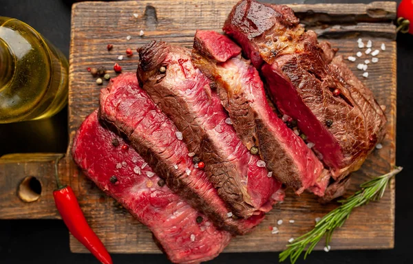 Siyah taş arka plan üzerinde ahşap doğrama tahtası üzerinde baharat ile Taze nadir ızgara beefsteak