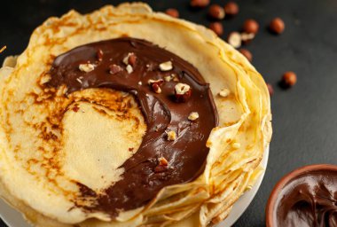 Siyah taş arka planda çikolatalı hamur ve fındık ile sunulan ev yapımı taze krep 