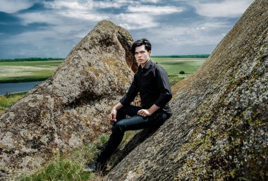 Siyah kıyafeti büyük kayalar üzerinde eğiliyor genç şık adam