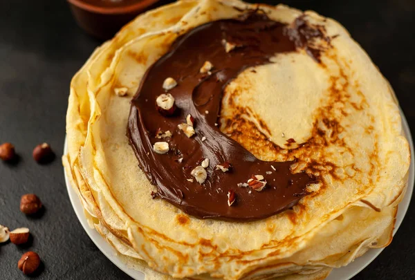 Homemade fresh crepes served with chocolate paste and hazelnuts on black stone background