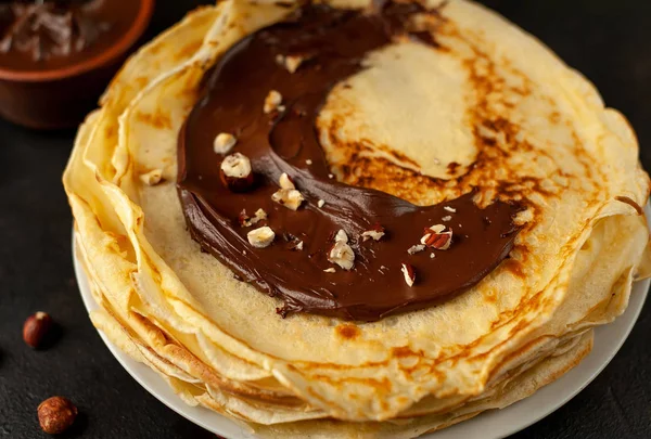 Homemade fresh crepes served with chocolate paste and hazelnuts on black stone background