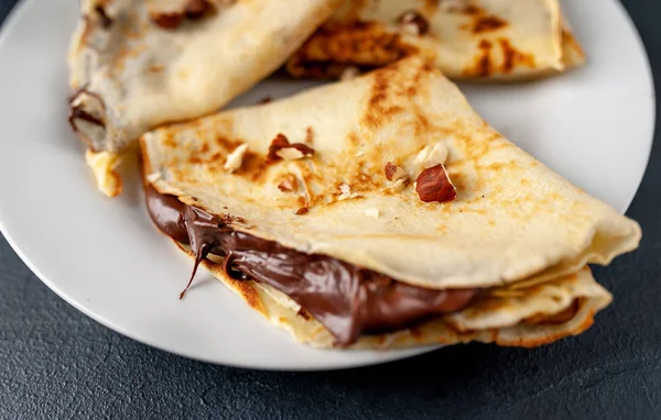 Homemade fresh crepes served with chocolate paste and hazelnuts on black stone background