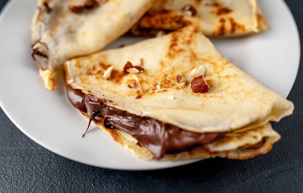 Homemade fresh crepes served with chocolate paste and hazelnuts on black stone background 