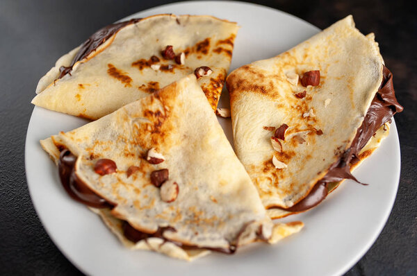 Homemade fresh crepes served with chocolate paste and hazelnuts on black stone background 