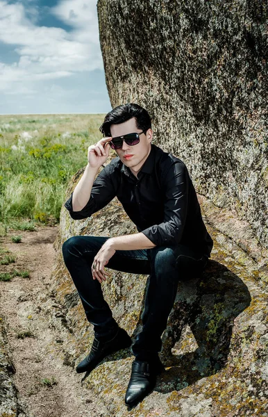 Young stylish man in black outfit leaning on huge rocks