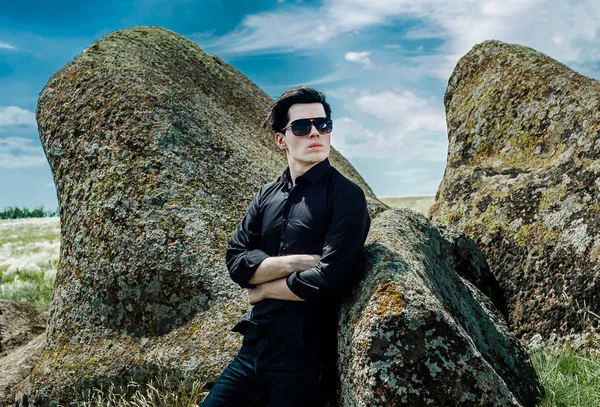 Young stylish man in black outfit leaning on huge rocks