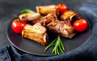 Siyah bir tabakta ızgara domuz kaburgası ve arka planda baharatlar. Metnin için kopyalama alanı var.