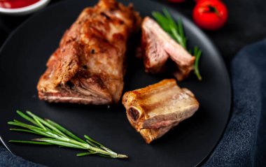 Siyah tabakta ızgara domuz kaburgası ve arka planda baharatlar.