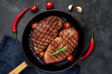 Bir tavada iki ızgara biftek ve arka planda baharatlar.