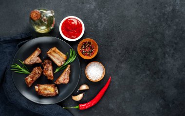 Siyah bir tabakta ızgara domuz kaburgası ve arka planda baharatlar. Metnin için kopyalama alanı var.