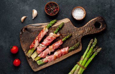 Pastırma ve baharatla pişirilmiş kuşkonmaz kesme tahtasının üzerinde.