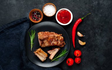 Siyah bir tabakta ızgara domuz kaburgası ve arka planda baharatlar. Metnin için kopyalama alanı var.