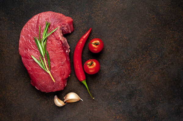 raw beef steak with spices and herbs on black slate background