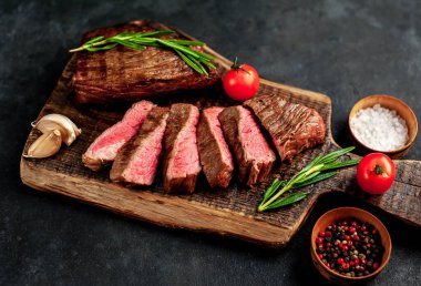 Baharatlı yağlı ızgara biftek, biberiye ve acı biber siyah taş arka planda doğrama tahtasında.