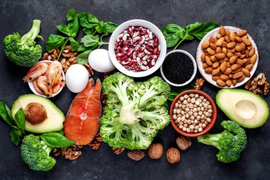 Kırmızı somonlu keto diyeti, taze sebzeler ve fındıklı meyveler ve siyah taş arka planda yeşillikler.