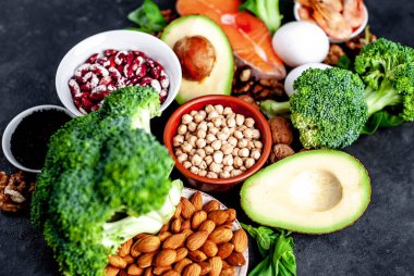 Kırmızı somonlu keto diyeti, taze sebzeler ve fındıklı meyveler ve siyah taş arka planda yeşillikler.