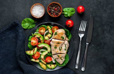 Domatesli tavuk, avokado dilimleri ve siyah tabakta yeşil salata. 