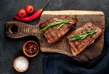 Baharatlı yağlı ızgara biftek, biberiye ve acı biber siyah taş arka planda doğrama tahtasında.