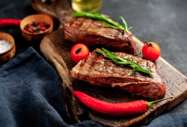 Baharatlı yağlı ızgara biftek, biberiye ve acı biber siyah taş arka planda doğrama tahtasında.