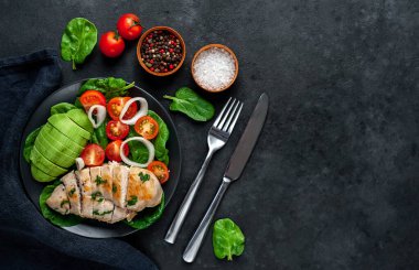 Domatesli tavuk, avokado dilimleri ve siyah tabakta yeşil salata. 