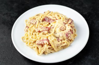 Pastırmalı spagetti ve siyah arka planda peynir.