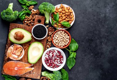 Kırmızı somonlu keto diyeti, taze sebzeler ve fındıklı meyveler ve siyah taş arka planda yeşillikler.