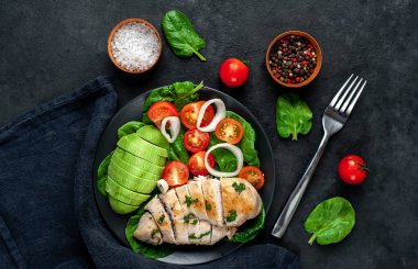 Domatesli tavuk, avokado dilimleri ve siyah tabakta yeşil salata. 