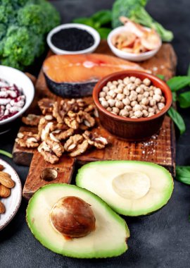 Kırmızı somonlu keto diyeti, taze sebzeler ve fındıklı meyveler ve siyah taş arka planda yeşillikler.