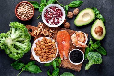 Kırmızı somonlu keto diyeti, taze sebzeler ve fındıklı meyveler ve siyah taş arka planda yeşillikler.