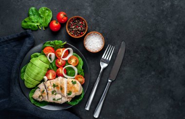 Domatesli tavuk, avokado dilimleri ve siyah tabakta yeşil salata. 