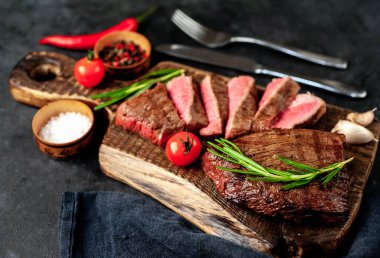 Baharatlı yağlı ızgara biftek, biberiye ve acı biber siyah taş arka planda doğrama tahtasında.