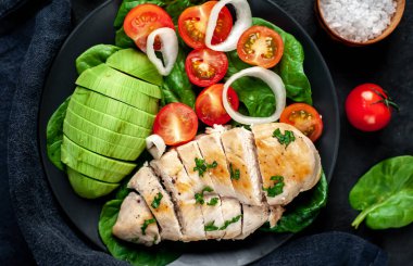 Domatesli tavuk, avokado dilimleri ve siyah tabakta yeşil salata. 