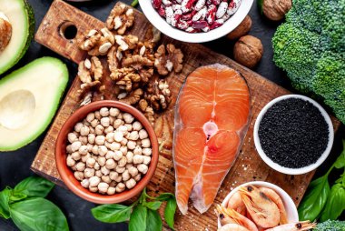 Kırmızı somonlu keto diyeti, taze sebzeler ve fındıklı meyveler ve siyah taş arka planda yeşillikler.