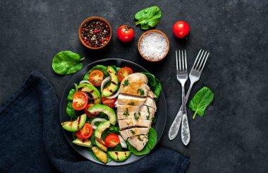 Domatesli tavuk, avokado dilimleri ve siyah tabakta yeşil salata. 