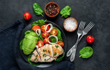 Domatesli tavuk, avokado dilimleri ve siyah tabakta yeşil salata. 