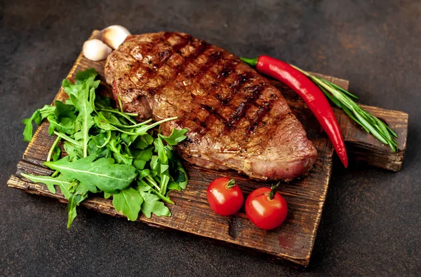 Fatty grilled beef steak with spices, rosemary and chili pepper on black stone background