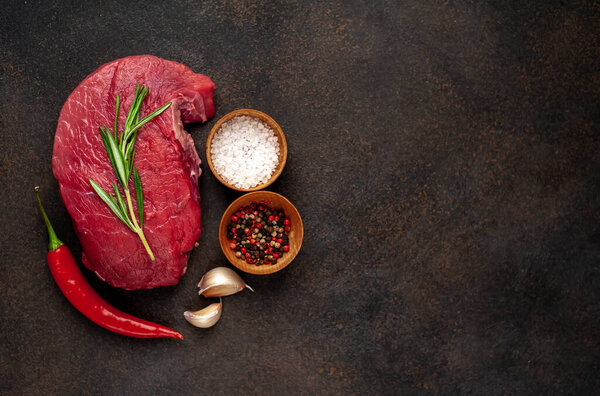 Fresh raw steak with rosemary twigs and spices on black background