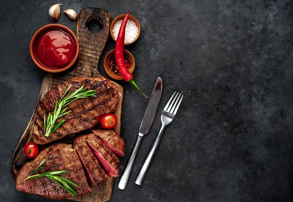 Fatty grilled beef steak with spices, rosemary and chili pepper on black stone background