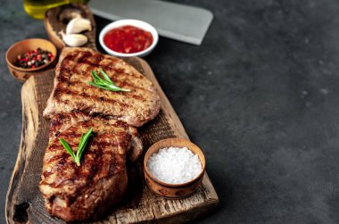 Ahşap kesme tahtasının üzerinde baharatlı, sebzeli ve otlu ızgara biftek..