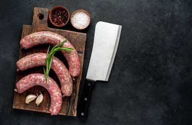 Ahşap kesme tahtasının üzerinde baharatlı ve otlu çiğ sosisler..